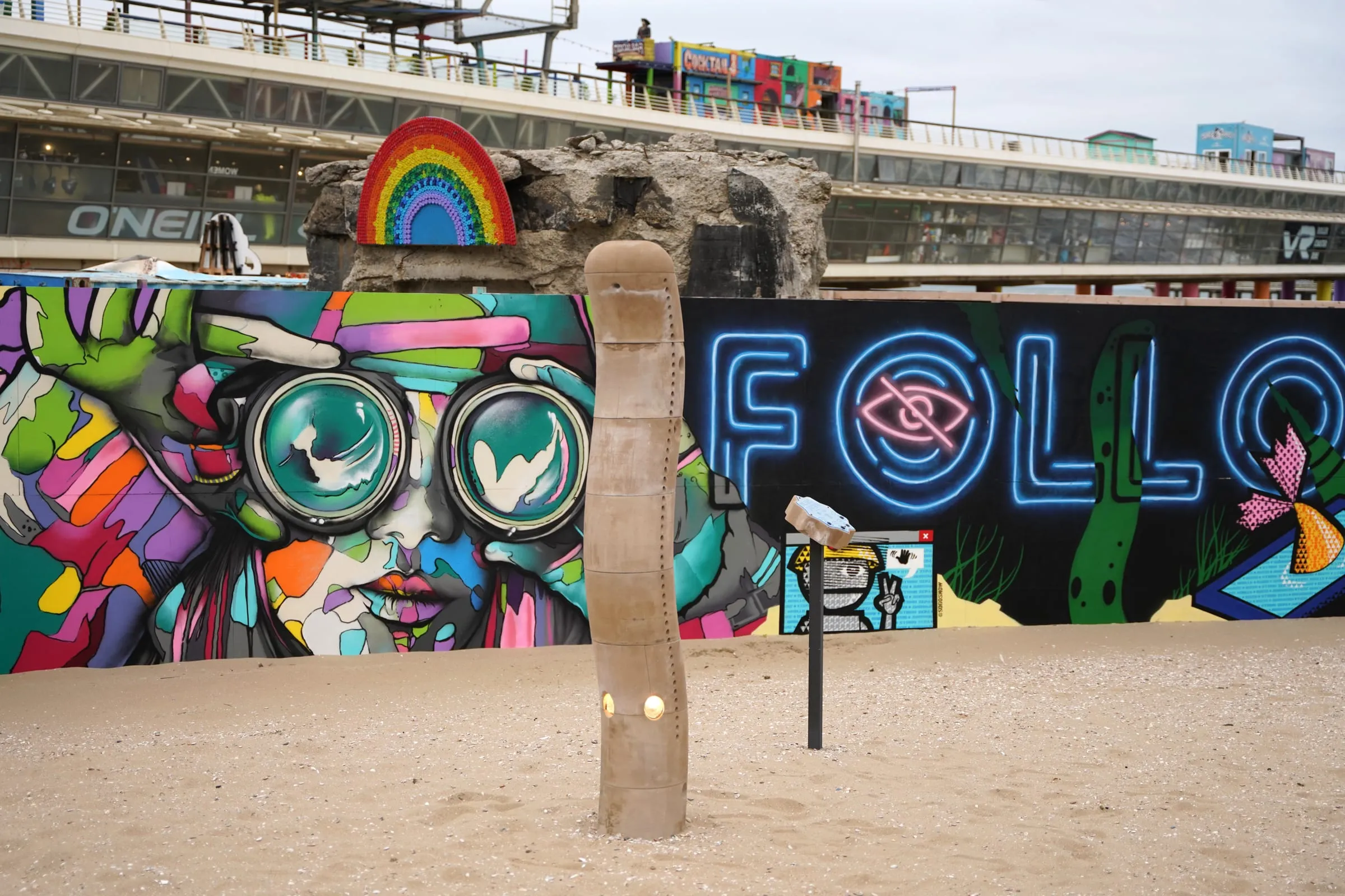 Wide view of the sculpture on the beach against the boulevard murals