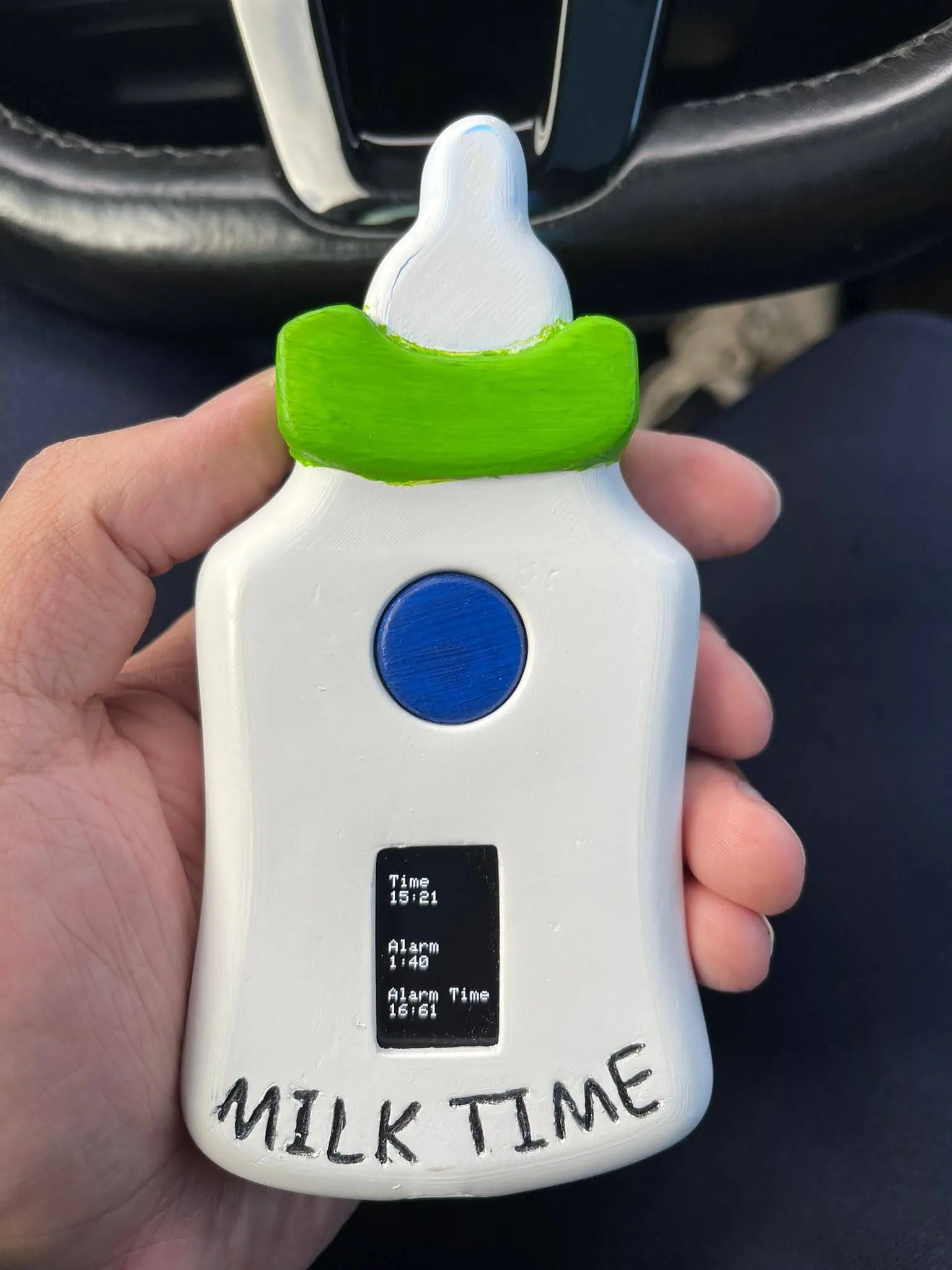 The finished Milk Time device, bottle-shaped with a blue button and a small display showing alarm times